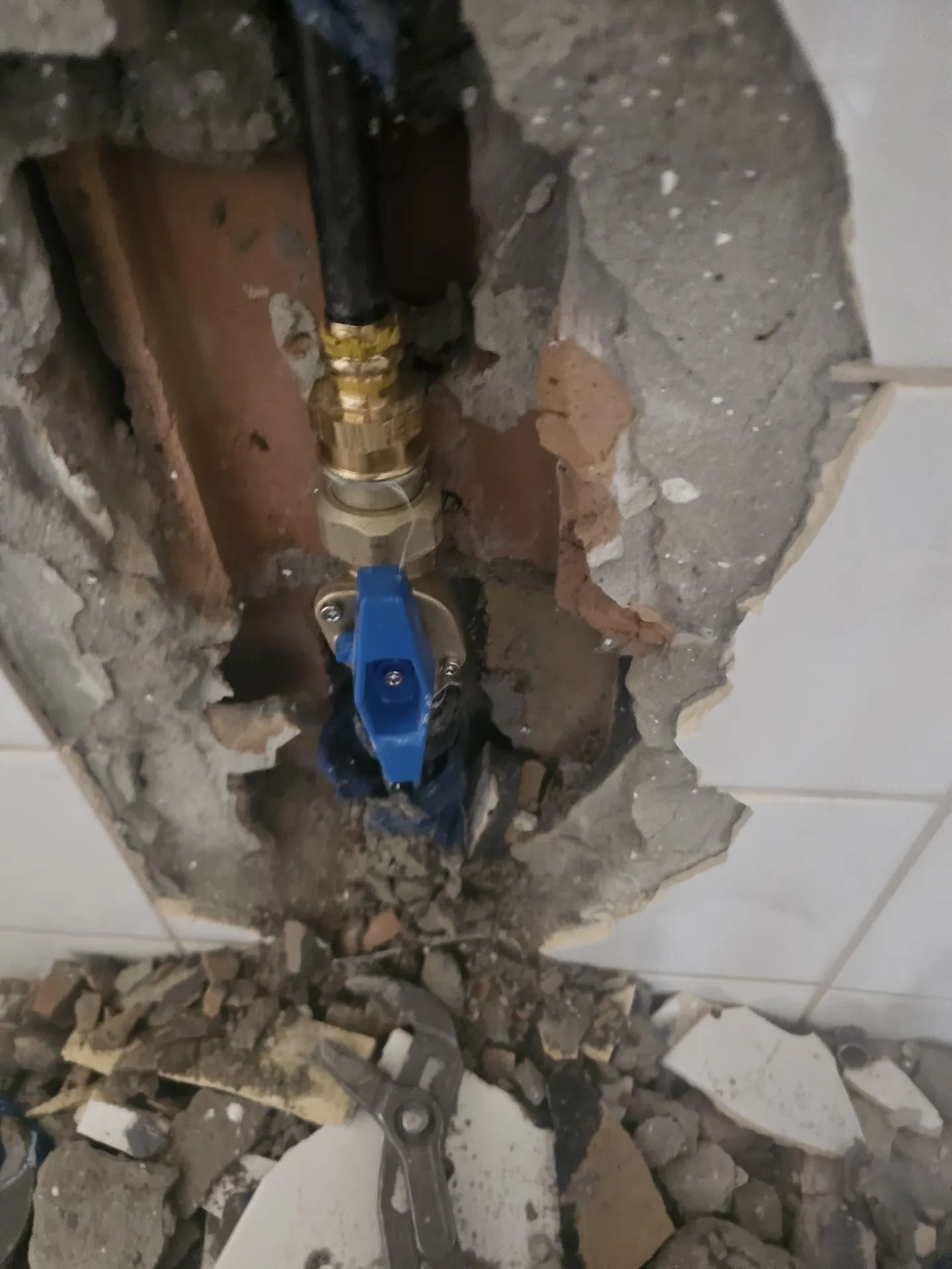 A képen egy épületgépészeti munka látható Öskü városában, ahol a falban lévő csövekhez és szelepekhez való hozzáférés érdekében falbontás történt. A képen jól látható a sérült fal, a mögöttes csővezetékek, valamint a szerelési munkákhoz használt eszközök. A HydroArt Kft. szakértelmét tükrözi az épületgépészet terén végzett munka.
