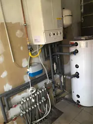 A képen az Öskü városában található HydroArt Kft. épületgépészeti rendszerének egy része látható. A falra szerelt bojler és a csővezetékek jól láthatóak, valamint a padlófűtéshez kapcsolódó elosztó egység. Az épületgépészet modern megoldásai tükrözik a cég szakértelmét és elkötelezettségét a minőség mellett.